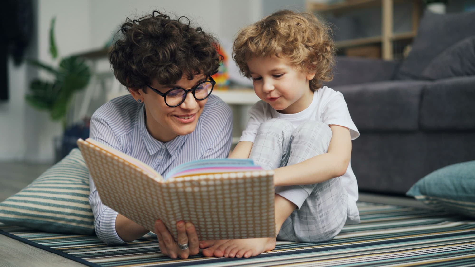 A parent and child reading a picture book on the floor together
